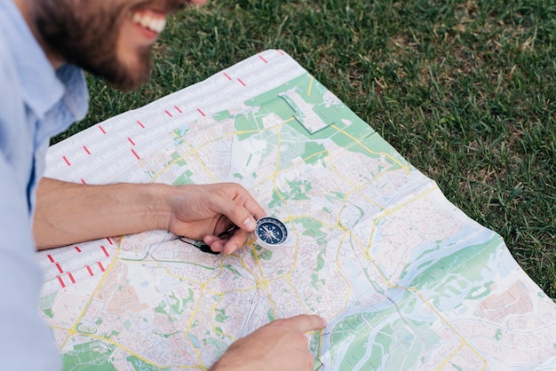 Smiling man holding compass and pointing at map on grass