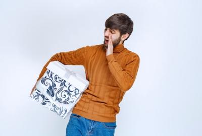 Man holding a white gift box with blue patterns making sound to notice someone