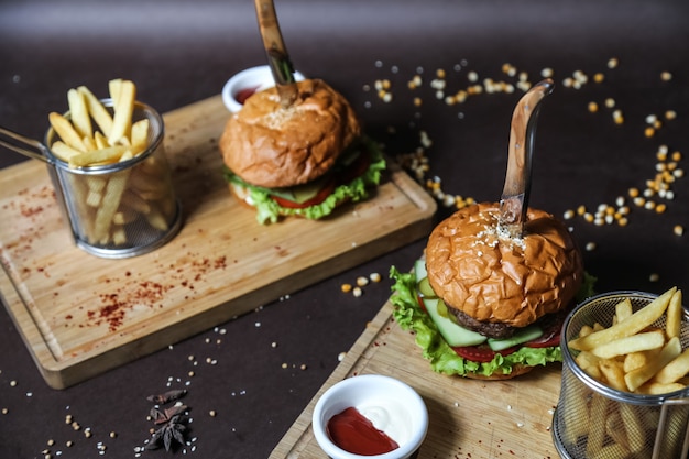 Delicious Meat Burger with Lettuce, Tomato, Cucumber, and French Fries on Wooden Board (Side View)