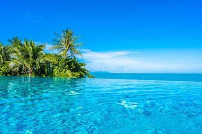 Beautiful luxury outdoor swimming pool in hotel resort with sea ocean around coconut palm tree and white cloud on blue sky