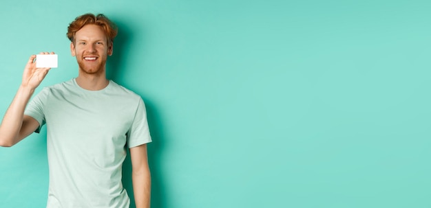 Handsome Redhead Man in Tshirt Showing Plastic Credit Card and Smiling While Shopping – Free Stock Photo Download