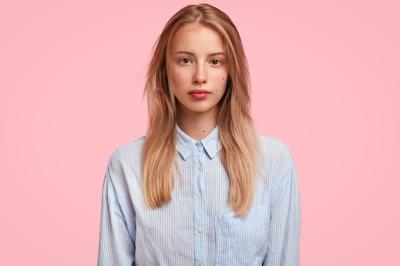 Adorable Caucasian young female with confident serious look, has long hair, dressed in stylish shirt, stands against pink wall, ready to talk with coworker