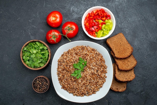 Top View Tasty Cooked Buckwheat with Dark Bread Loafs and Greens on Dark Space