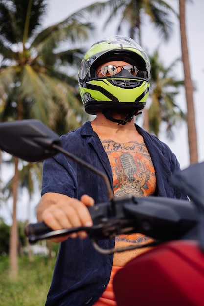 Tattooed strong man on tropical jungle field with red motorbike