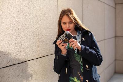 Happy hipster girl taking photo with retro camera on city street. Travel concept