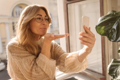 Cute Caucasian Adult Blonde Lady in Warm Sweater Sending Air Kiss to Phone Selfie Time Concept