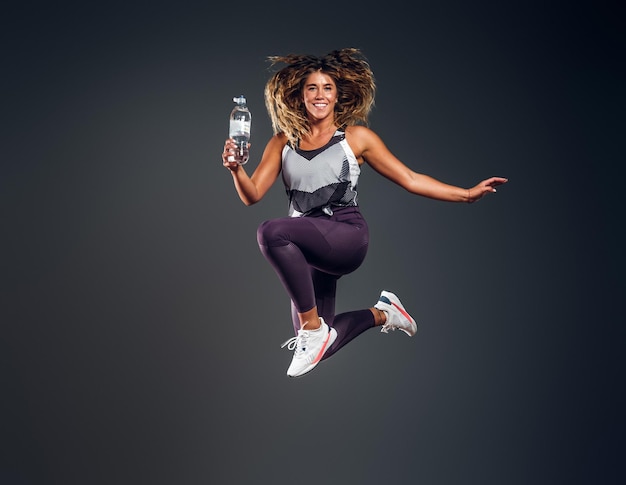 Excited Woman Jumping in Studio with Water Bottle