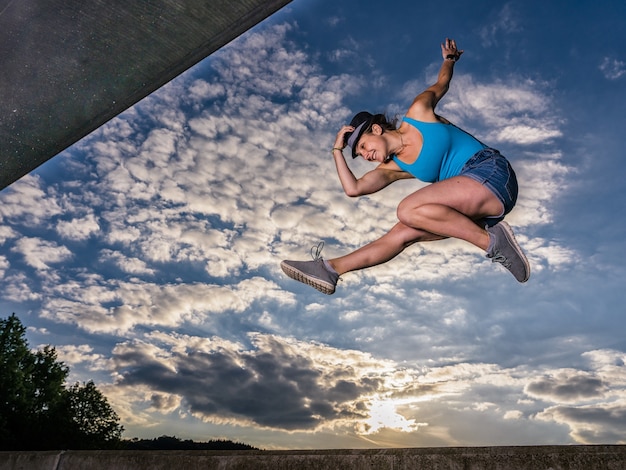 Sporty European female jumping up in the air on cloudy sky background