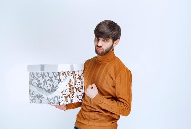 Man holding a white gift box with blue patterns and showing satisfaction sign