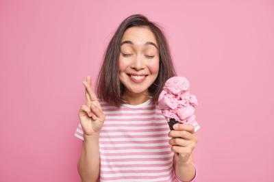 Woman Believes in Good Fortune Keeps Fingers Crossed Closes Eyes Smiles Pleasantly Wears Casual Striped T Shirt Holds Appetizing Ice Cream