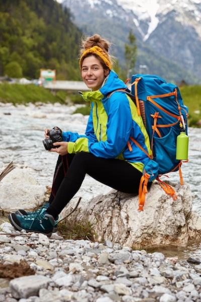 Tired Female Tourist Sitting by Stream in Mountains Holding Camera – Free Stock Photo Download