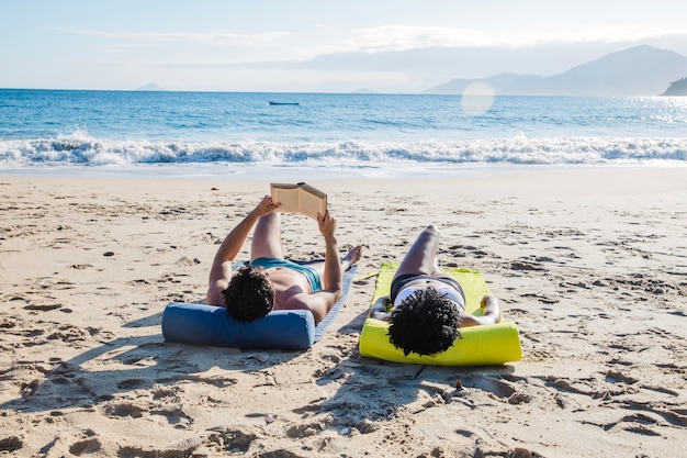 Couple reading and lying at the beach | Download Free Stock Photo