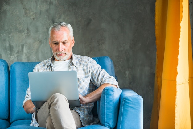 Elderly Man Sitting on Blue Sofa Using Laptop