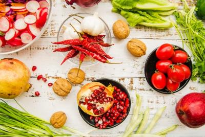 Elevated view of cherry tomato, red chilies, spring onion, garlic, chard leaves, parsley, ripe pomegranate and walnut