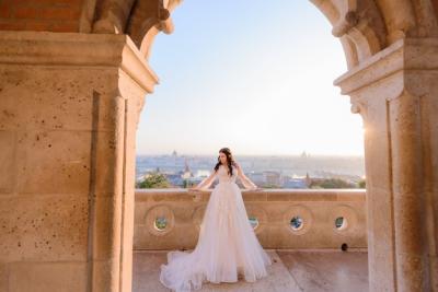 Tender Bride in Fashionable Wedding Dress Standing on Balcony of Old Stone Building