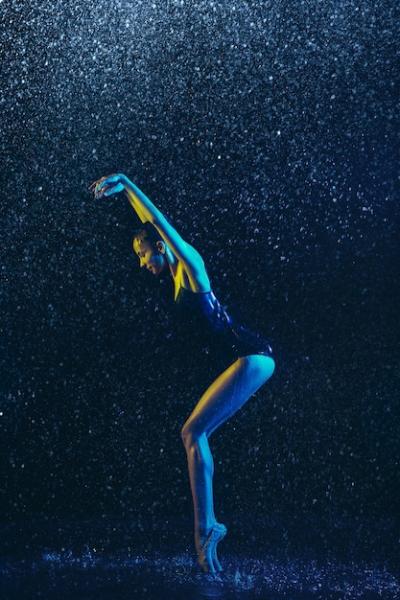 Young female ballet dancer performing under water drops and spray. Caucasian model dancing in neon lights. Attractive woman.