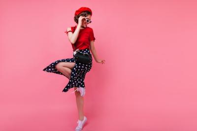 Excited brunette lady in black skirt dancing on rosy wall. Appealing white girl in french beret jumping.