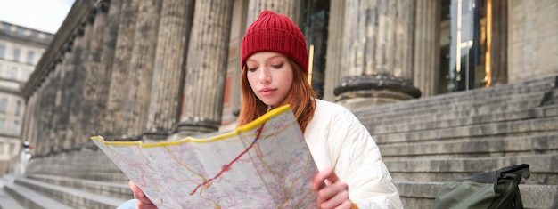 Tourism and Lifestyle Concept: Young Redhead Woman Planning Sightseeing Route with City Map