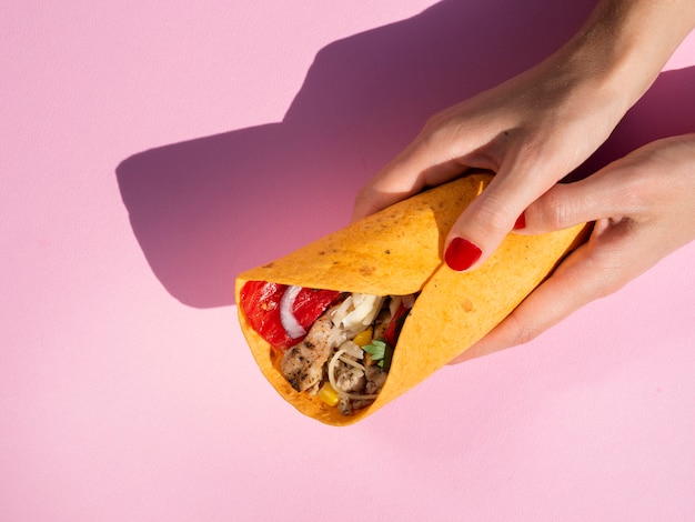 Close-up woman holding burrito with pink background