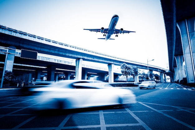 Blurred city street scene with a plane flying overhead