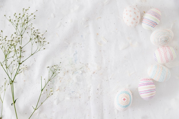 Row of Easter eggs with patterns near plant twig and feathers on textile – Free Stock Photo