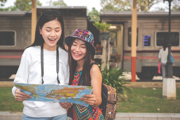 Two women holding a map while waiting for the train. Tourism concept