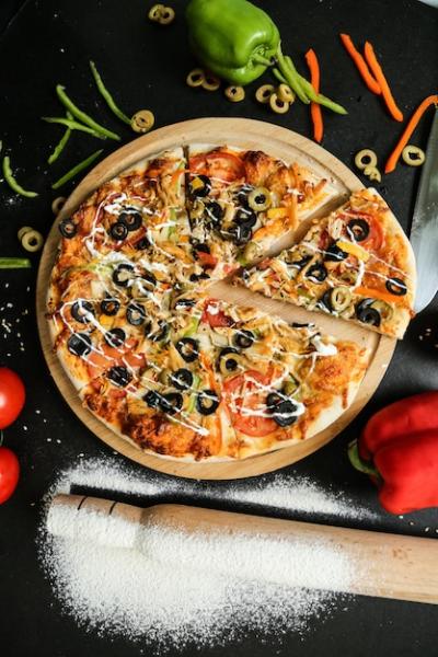 Top view pizza with olives, tomatoes, bell pepper, and rolling pin with flour