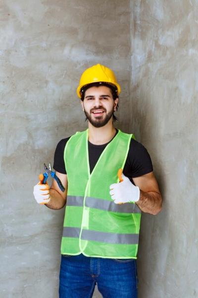 Engineer in Yellow Helmet and Industrial Gloves Holding Blue Pliers and Showing Thumb Up Sign