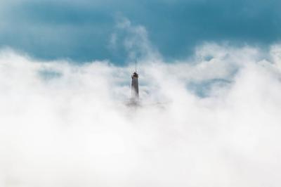 Wide Shot of a Lighthouse Covered in White Clouds in a Blue Sky