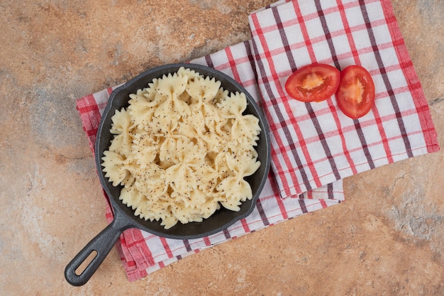 Farfalle on black pan with tomato slices