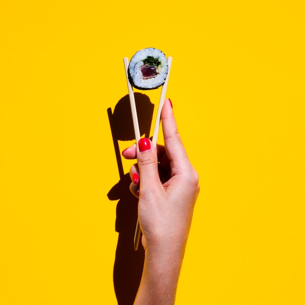 Woman holding chopsticks with sushi roll on yellow background