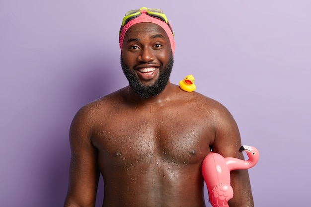 Candid shot of smiling dark skinned guy with toothy smile, has white teeth, enjoys swimming and summer rest, carries swim ring for free download