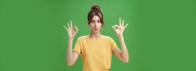 Portrait of Silly, Cute, and Beautiful Caucasian Woman with Combed Hair in Round Earrings and Yellow T-shirt Showing Ok Gesture over Green Wall