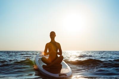 Silhouette of beautiful woman practicing yoga on surfboard at sunrise