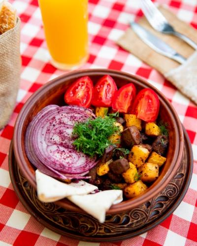 Fried meat with potatoes served with onions tomatoes and greens