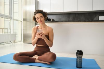 Yoga and sport at home concept young woman sitting in bright room with mobile phone doing workout