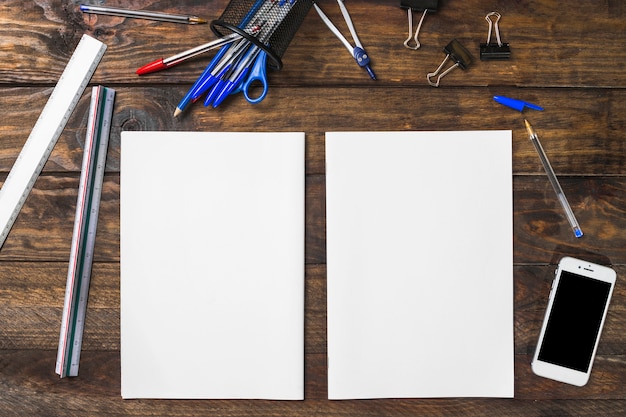 White blank paper surrounded with stationeries and smartphone on wooden table – Free Stock Photo