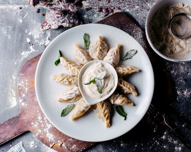 Dough Dish with Meat, Green Leafs, and Sour Cream on Brown Wooden Surface