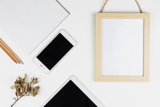 Tablet near smartphone, paper, pencils and photo frame