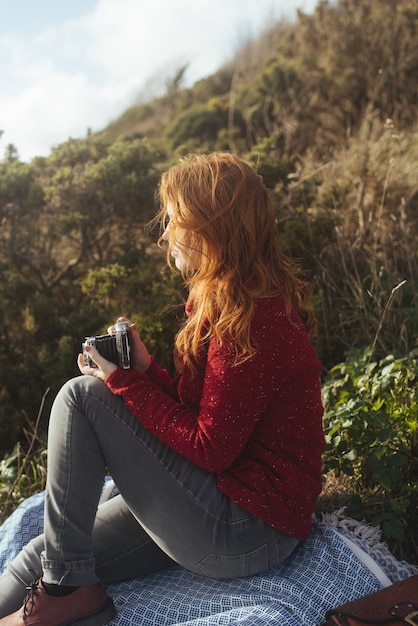 Vertical Shot of a Woman Sitting on a Blanket By the Trees and the Sea