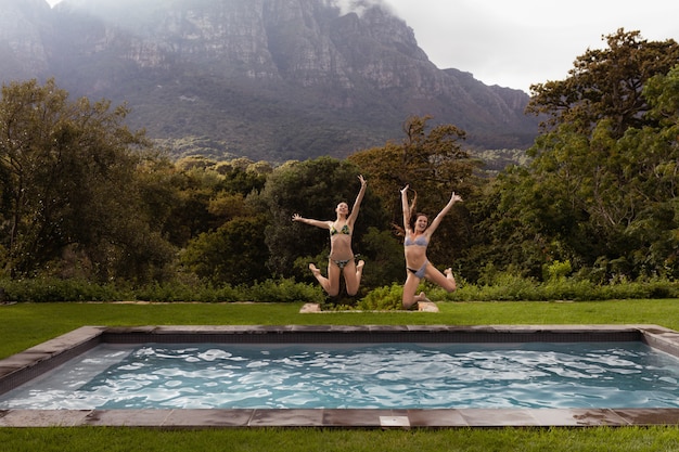 Female friends jumping in swimming pool at backyard – Free Stock Photo