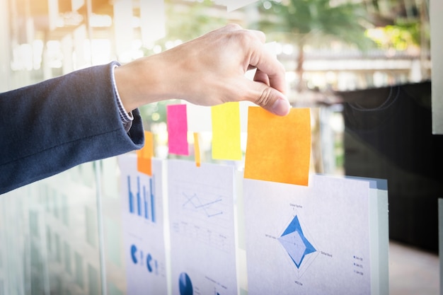 Close up shot of hands of business man sticking adhesive notes on glass wall in office