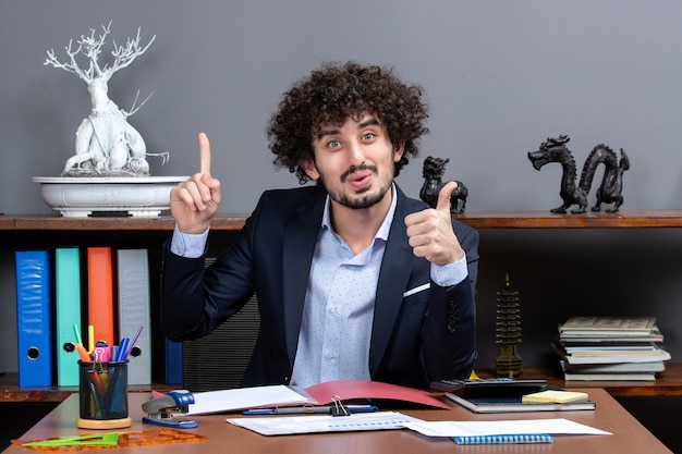 Front view cool office worker giving thumbs up sitting at the desk in office