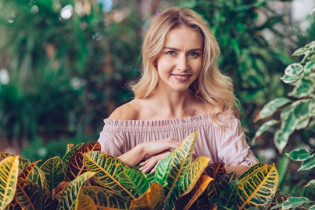 Blonde Young Woman Standing Behind Garden Croton Leaves