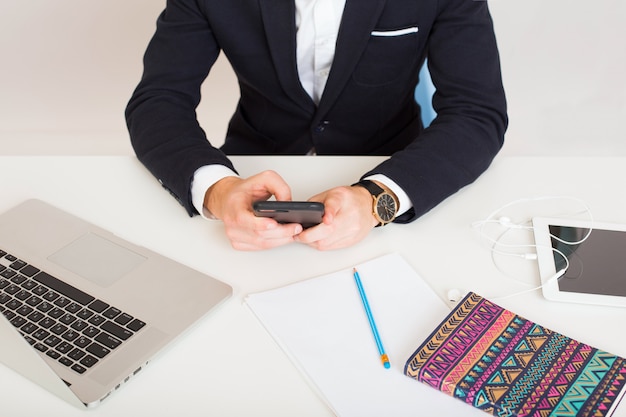 Young man in black jacket holding smartphone at office table