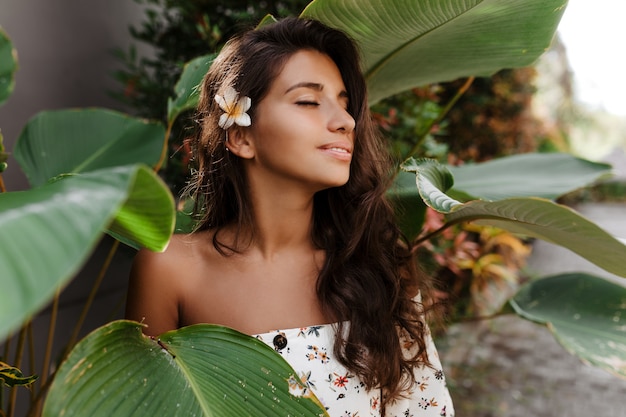 Close-up portrait of pacified woman with flower in dark wavy hair