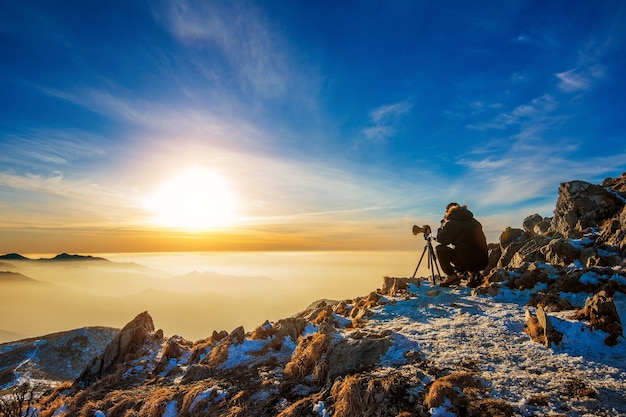 Professional Photographer Capturing Photos on Camera Tripod at Rocky Peak During Sunset