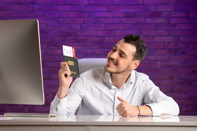 Front view office worker sitting behind his working place holding tickets and passport