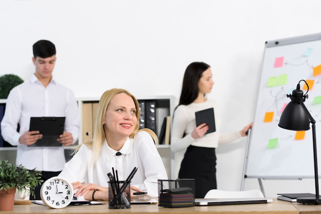 Male and female colleagues behind smiling businesswoman at workplace