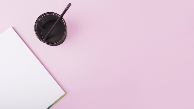 Elevated View of Notebook and Plastic Cup with Pencil on Pink Backdrop